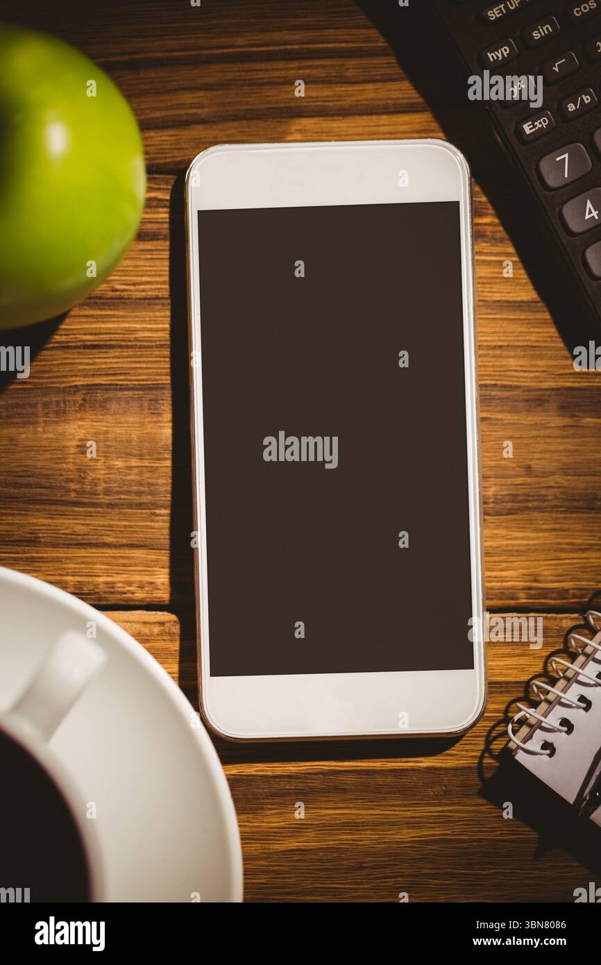 White smartphone is lying on tabletop in flat design, showing blank black screen, cup and notebook Stock Photo