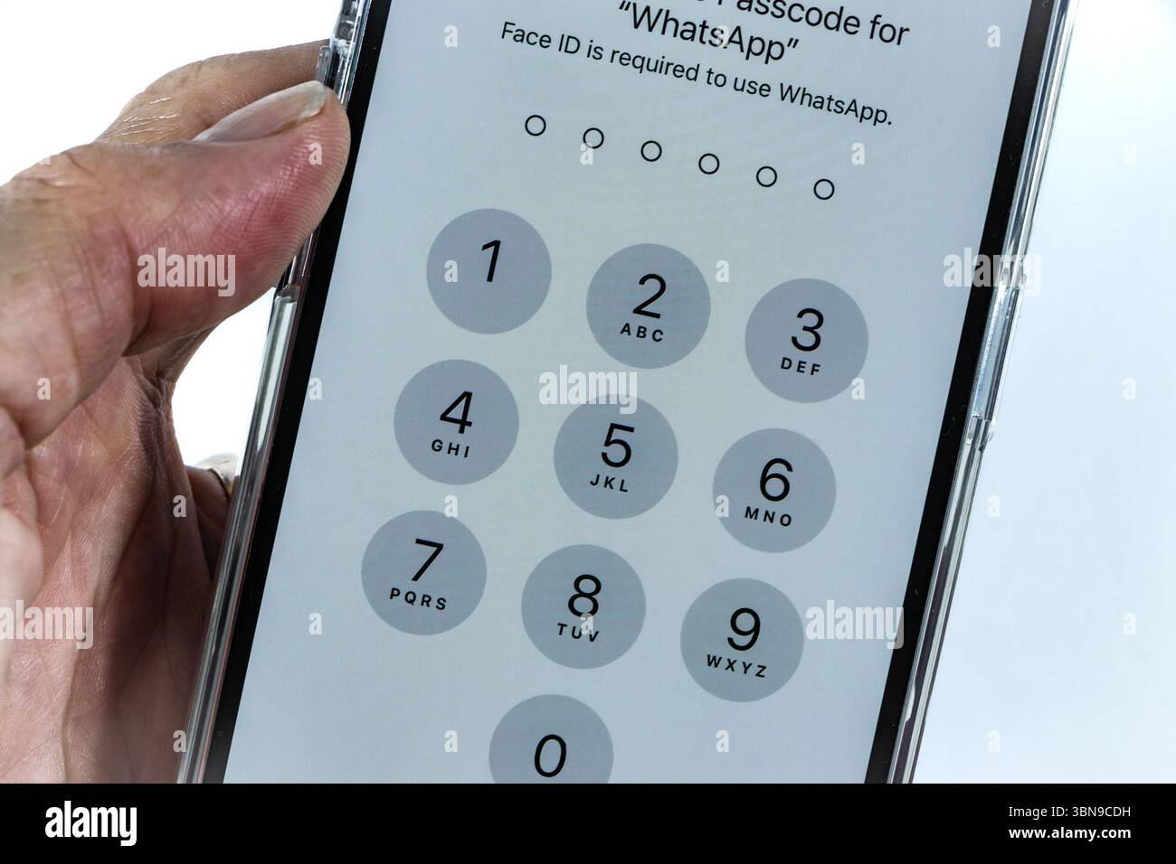 Close-up of a person holding a smartphone displaying a numeric keypad for WhatsApp passcode entry with Face ID requirement on iPhone 14 Pro Stock Photo