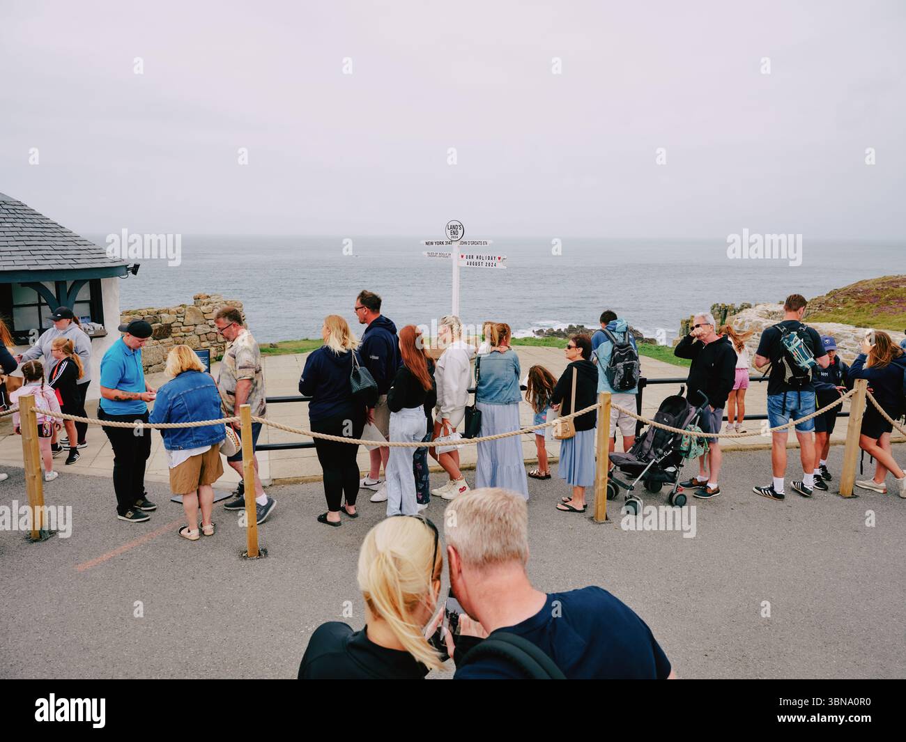 The queue for the famous Lands End signpost photograph at Lands End Cornwall England UK - tourism tourist  tourists cloudy weather Stock Photo
