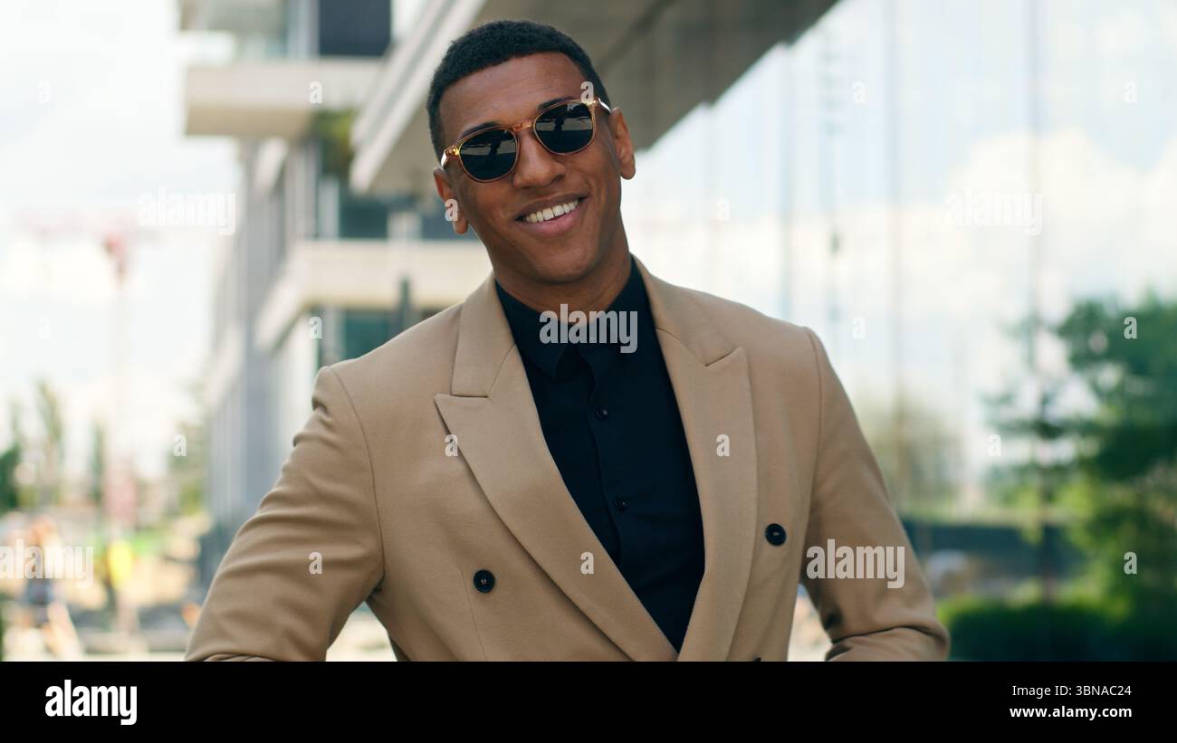 Smiling stylish fashionable confident African American business man posing in city outdoors wearing black sunglasses businessman guy male entrepreneur Stock Photo