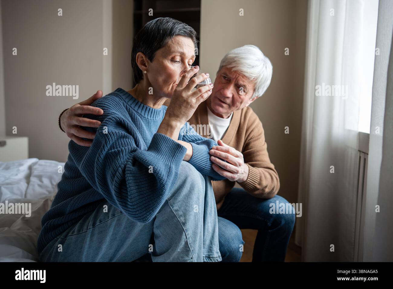 Distressed mature woman in emotional breakdown drinking water, receiving solace from senior partner Stock Photo