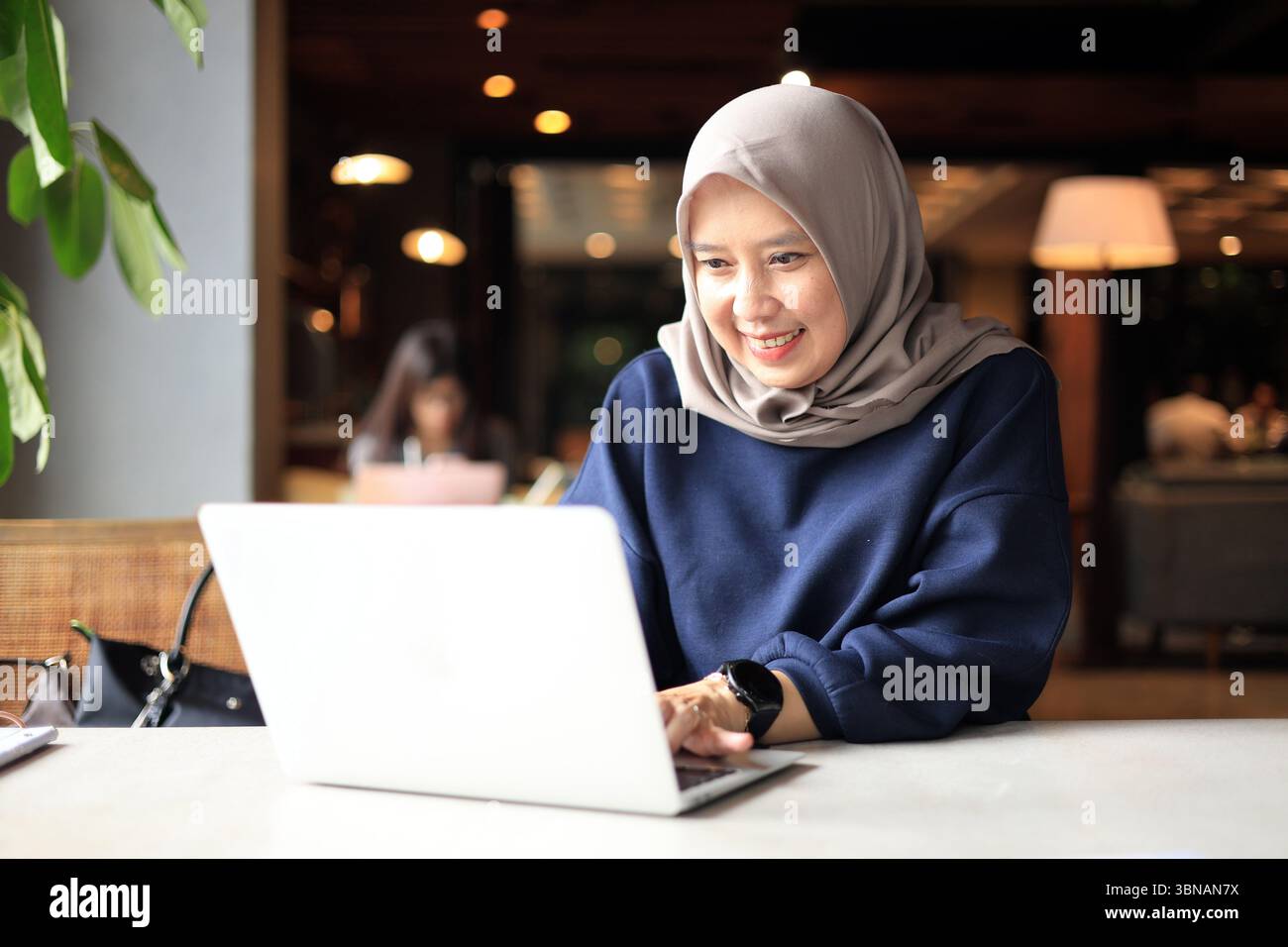 Middle Age Muslim Asian Women with Hijab Working at a Cafe and using Laptop Computer. Stock Photo