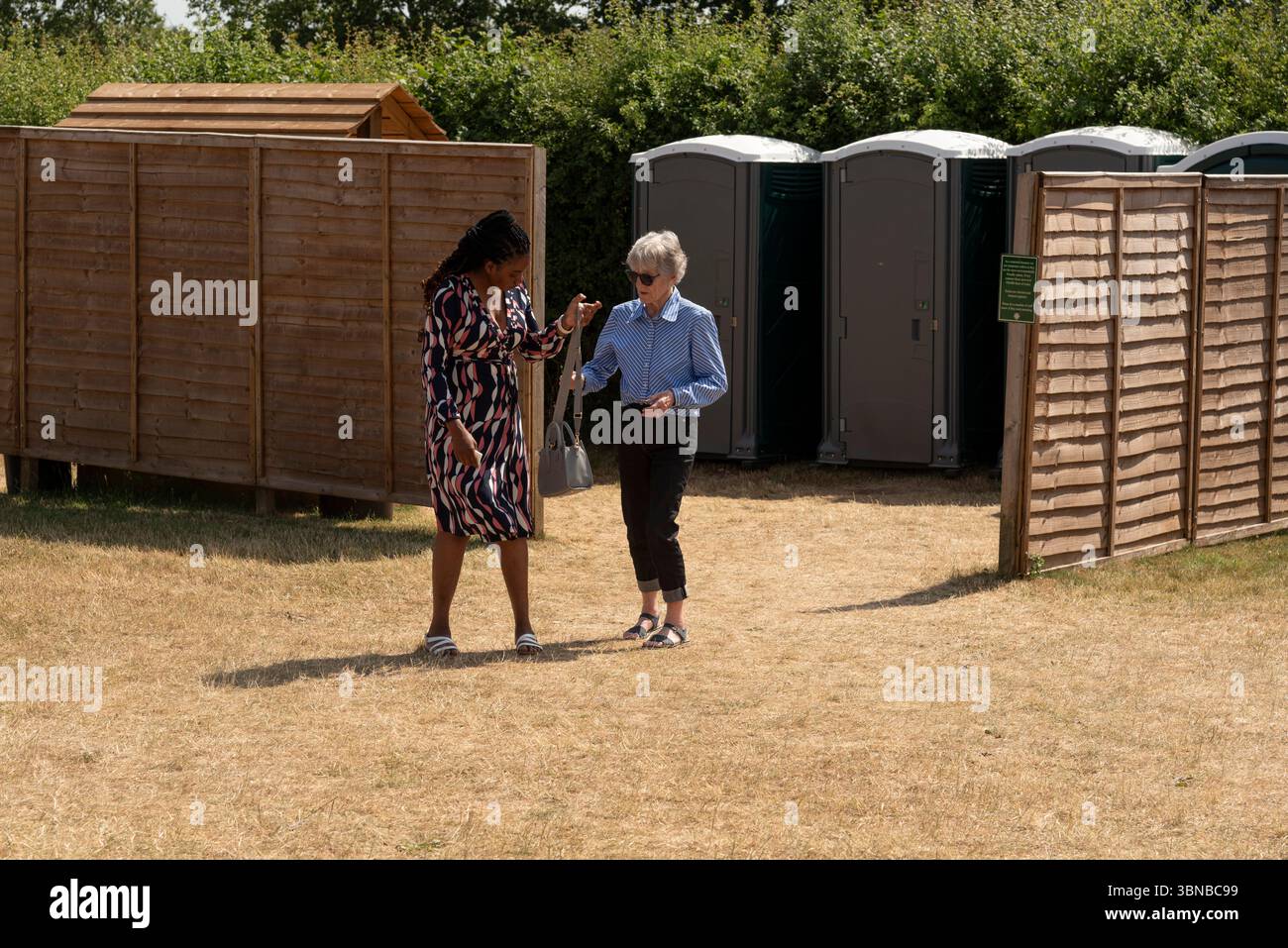 Gloucestershire England UK. 30.06.2025. Carer and patient on a countryside outing with a background of  toilet facilities outside block  fenced for p Stock Photo