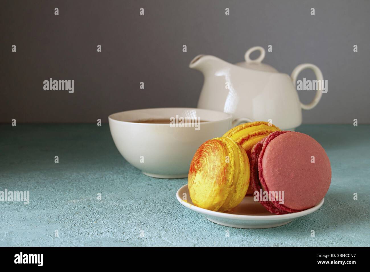 Colored macaroons and a teapot with a cup on a blue table Stock Photo