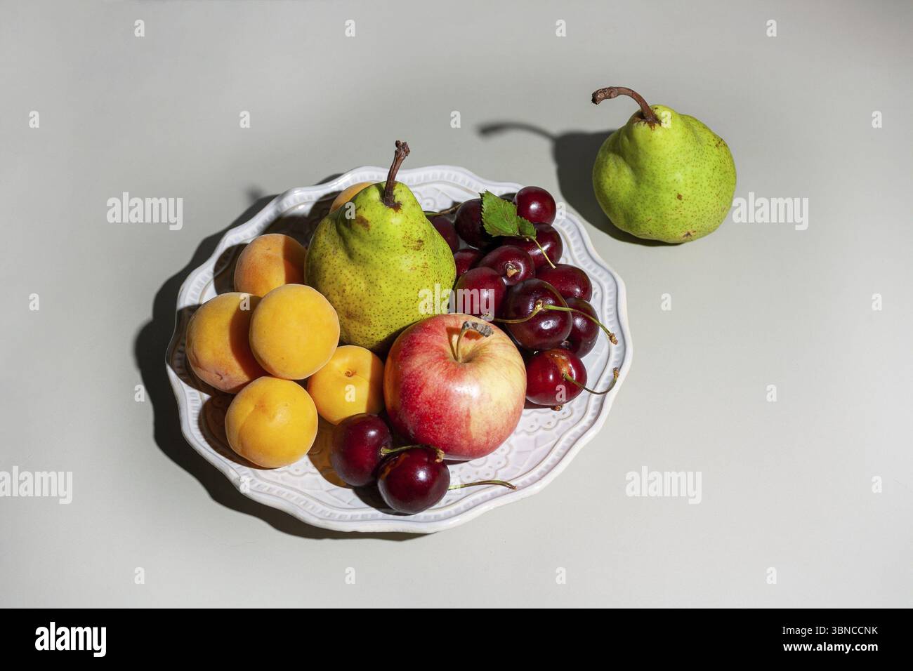 Fruits on white ceramic plate with hard shadow on gray background, selective focus Stock Photo