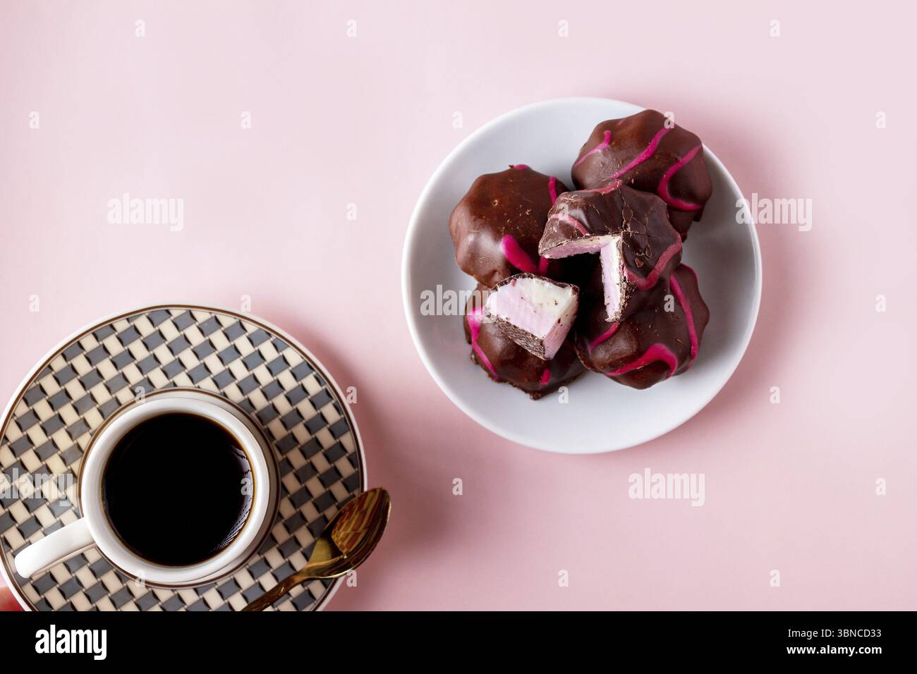 Plate with chocolate marshmallows and a cup of coffee on a pink background Stock Photo
