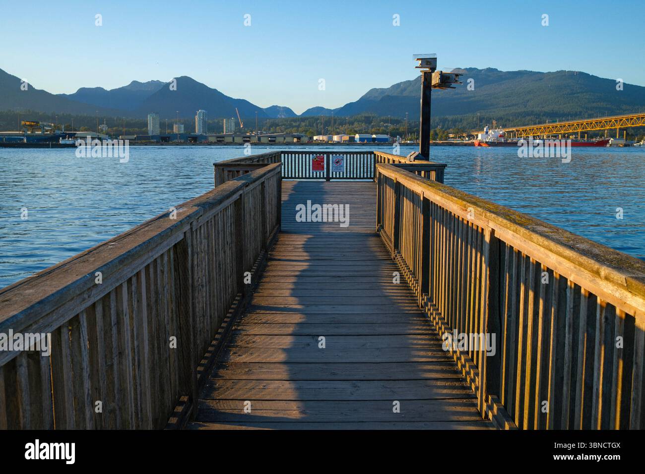 A wooden pier stretching into the Burrard Inlet at New Brighton Park with the Second Narrows Bridge to the right, Vancouver, BC. Stock Photo