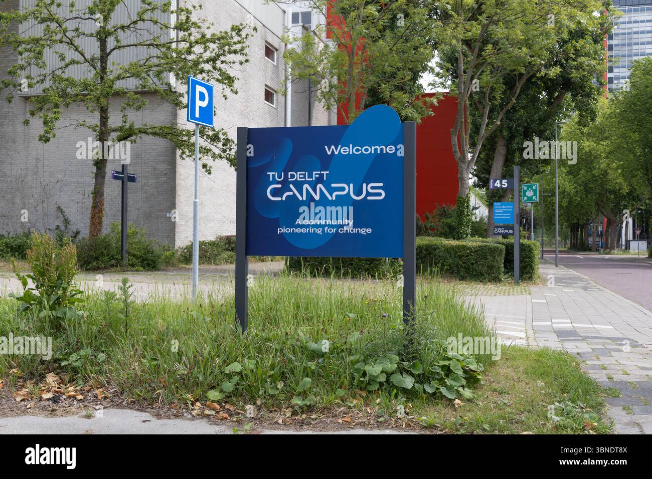A prominent "Welcome TU Delft Campus" sign, featuring the university's motto "A community pioneering for change." Stock Photo