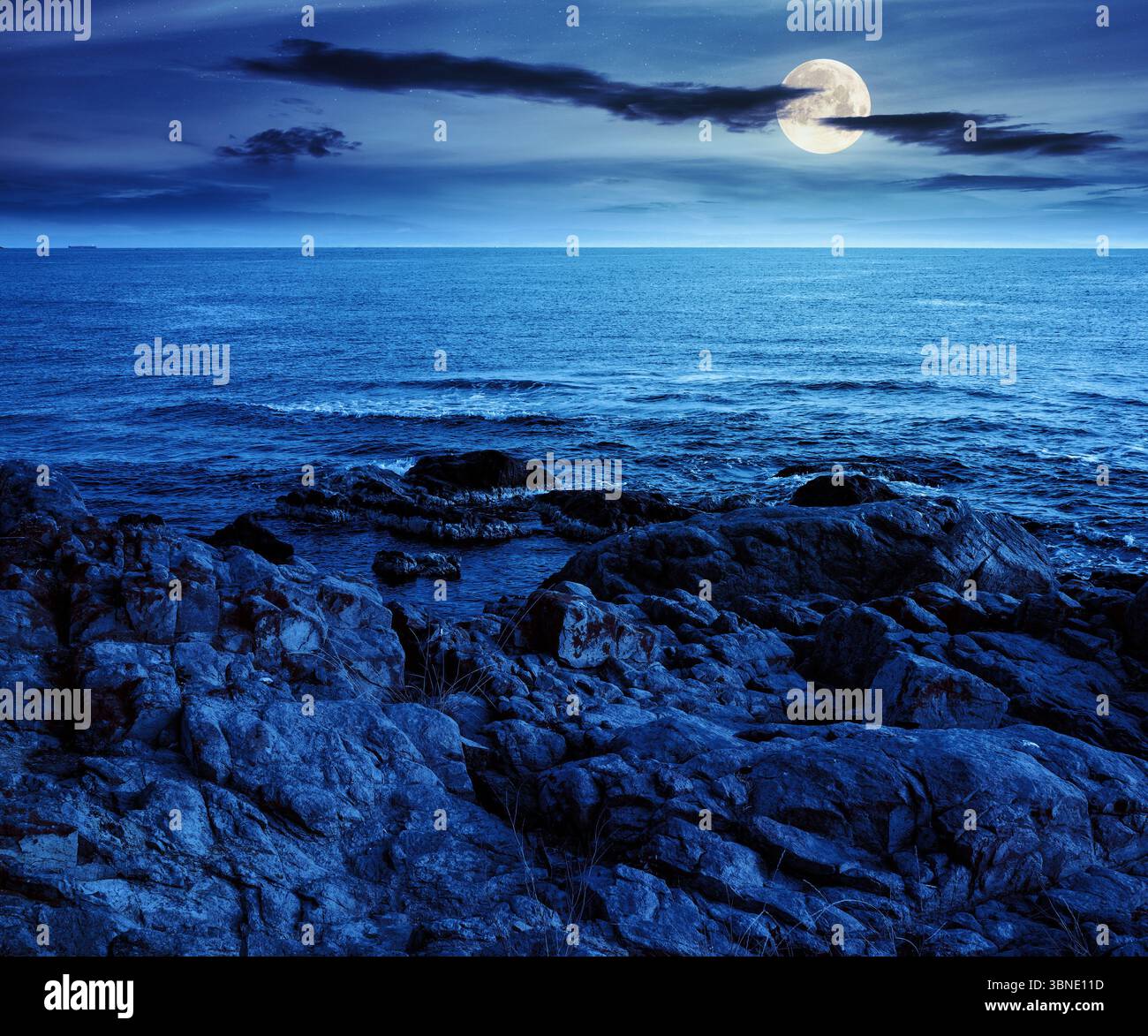 landscape of sea coast with rock in summer at night. beautiful scenery with stone shore and splashing wave in full moon light. mysterious scene in bul Stock Photo