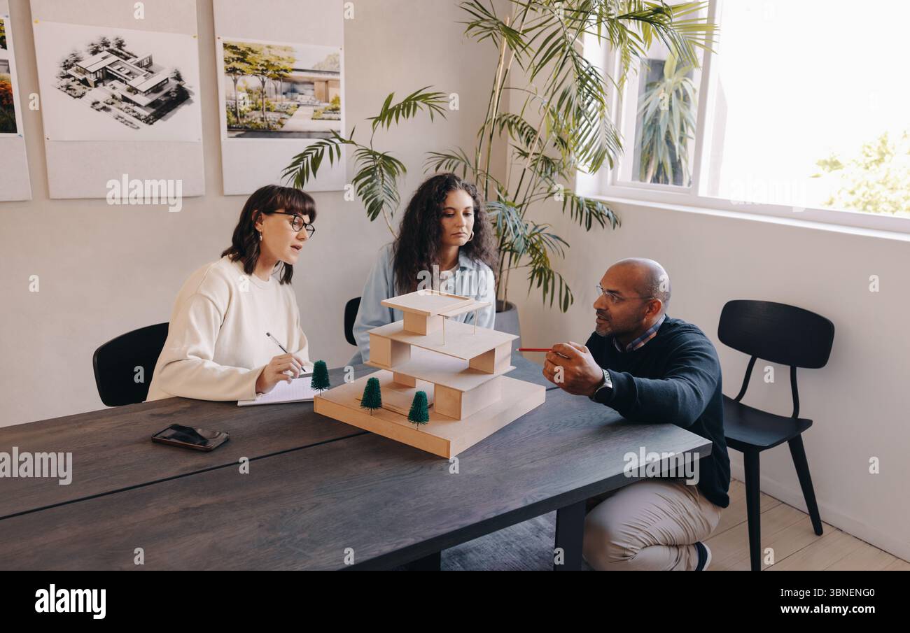 Three architects in a modern office collaborate on a project around a scale model, planning. Stock Photo