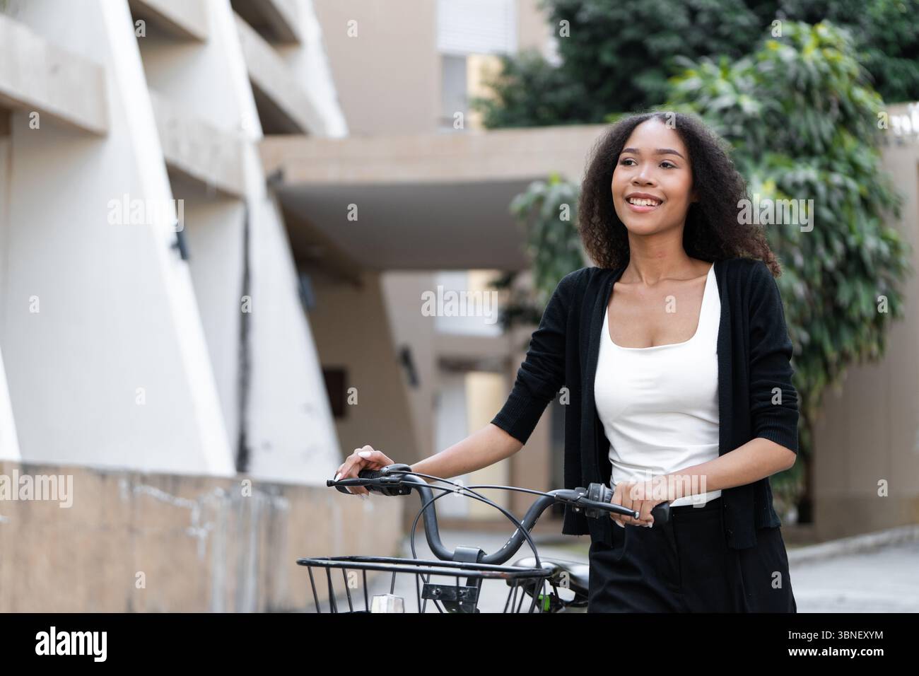 Sustainable Living and Eco-Friendly Transport. A young woman smiles while cycling, promoting a green lifestyle in an urban setting. Stock Photo