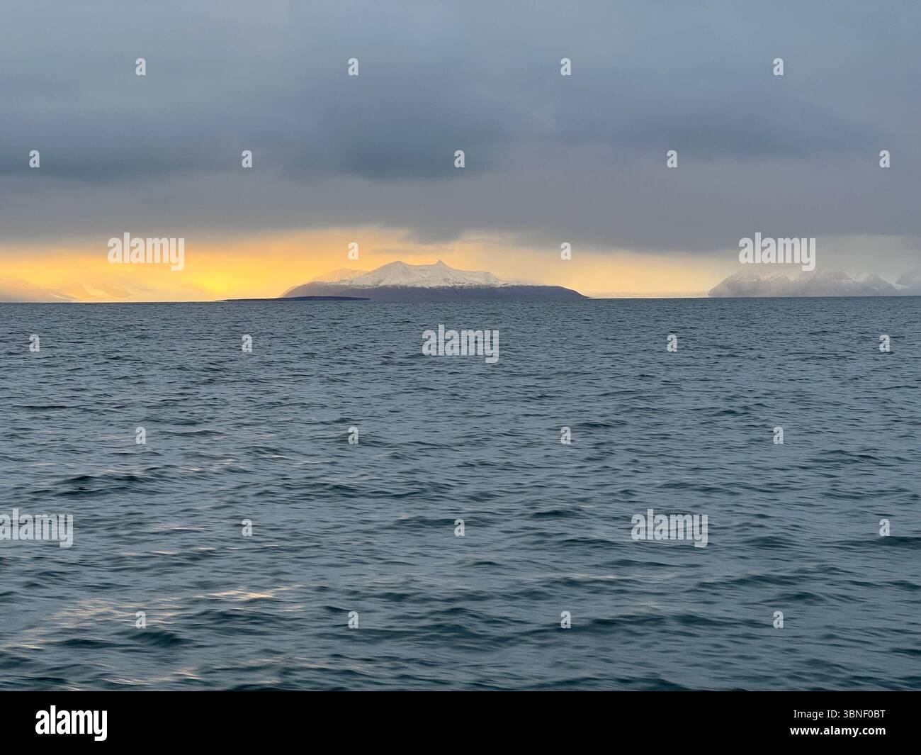 The island with snowy mountains is set against a beautiful cloudy sky over the ocean outside Longyearbyen, Svalbard - Smartphone Captured Stock Image
