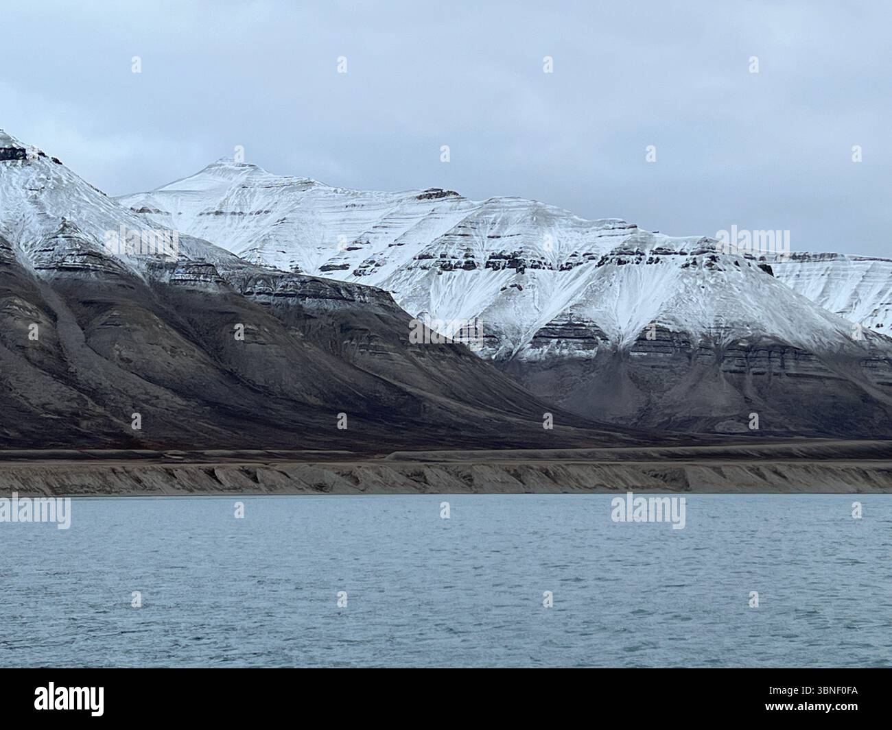 Majestic snow-covered mountains reflect in the tranquil water of a fjord. Spitsbergen, Svalbard - Smartphone Captured Stock Image