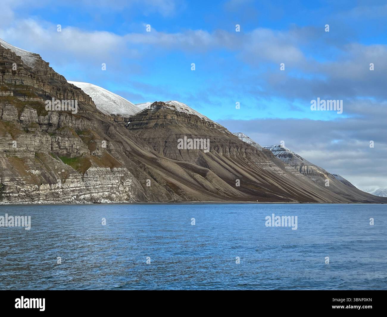 A stunning view of a mountain range next to a calm lake under a blue sky, Spitsbergen, Svalbard - Smartphone Captured Stock Image