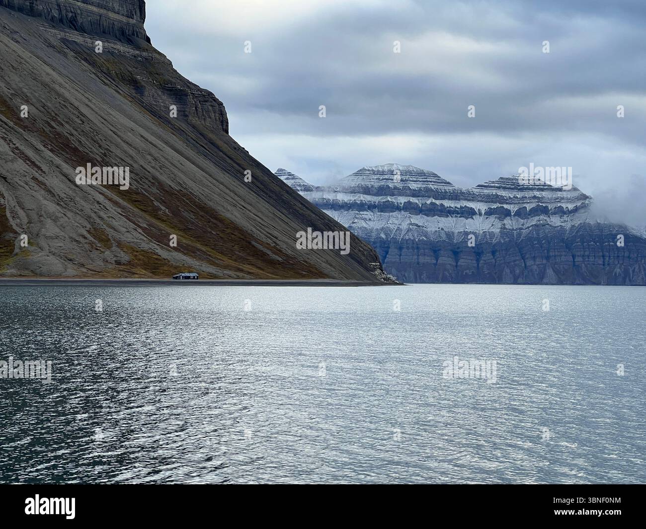 A stunning view of a mountain range next to a calm lake under a blue sky, Spitsbergen, Svalbard - Smartphone Captured Stock Image