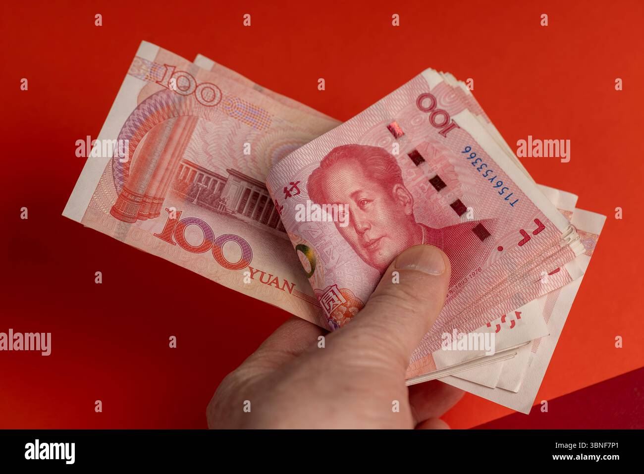 holding a stack of Chinese yuan in his hand on a red background, holding a  large amount of money in yuan in the hands of a man Stock Photo - Alamy
