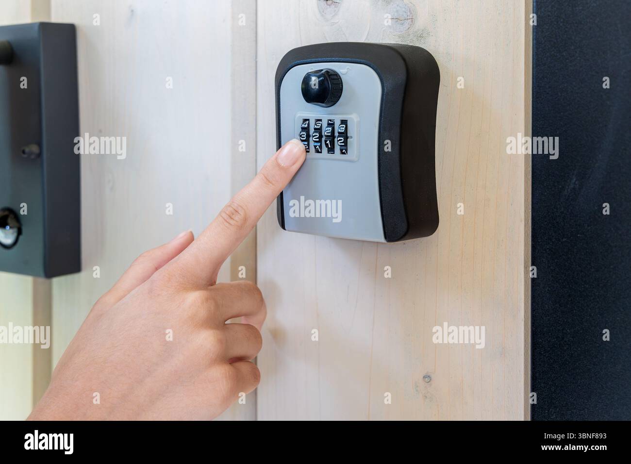 Hand Entering Code on Wall-Mounted Lockbox. Close-up of a person entering a numeric code on a combination key lockbox mounted to a wooden wall for Stock Photo