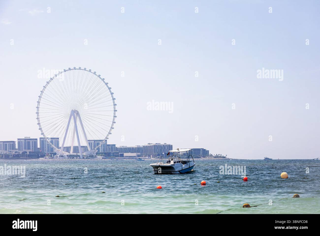 Dubai, United Arab Emirates - March 13, 2025: Boat gliding through ocean waters with a prominent Ferris wheel and city skyline in the background Stock Photo