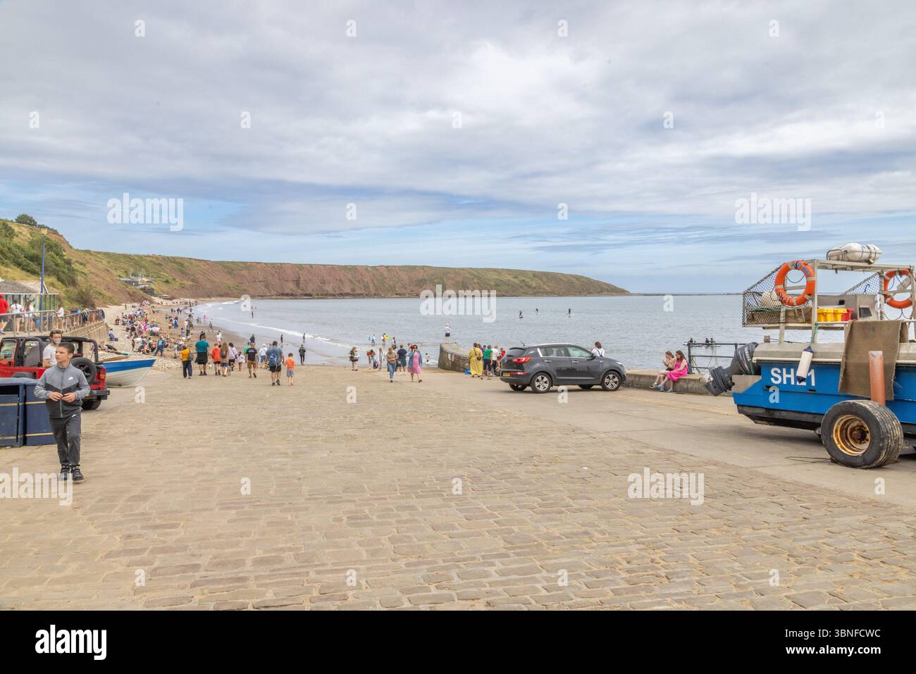 Visitors gather on Coble Landing, the slipway leading to the beach and sweeping curve of Filey Bay. Travel and tourism, North Yorkshire, UK. Stock Photo