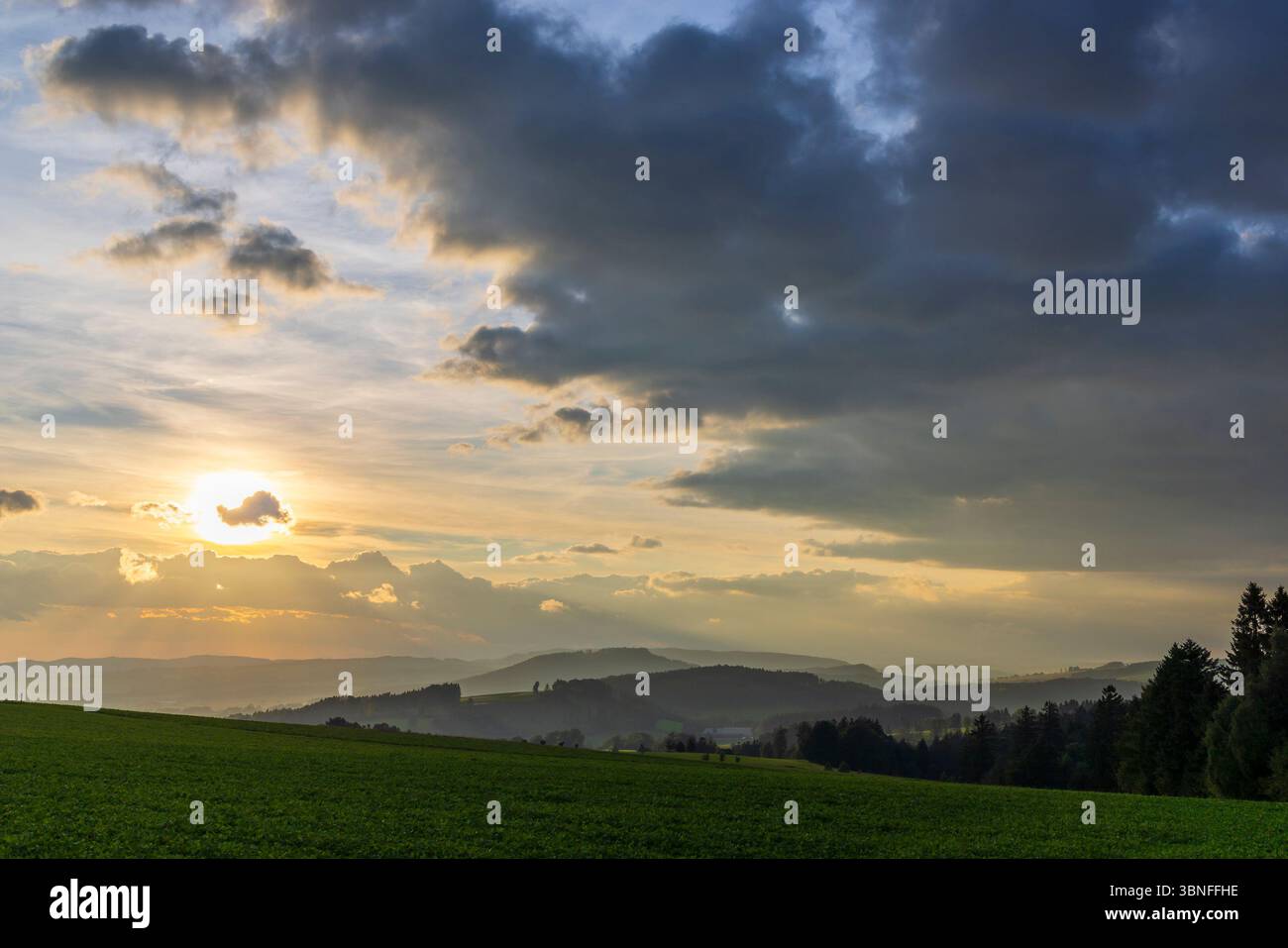 Sun setting behind clouds over rolling hills in Chvalec, Czechia Stock Photo