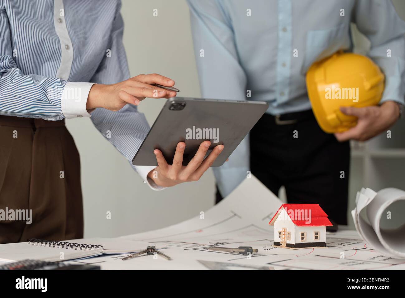 Collaboration and Construction Planning. Professionals discussing architectural plans while using a tablet for project management. Stock Photo