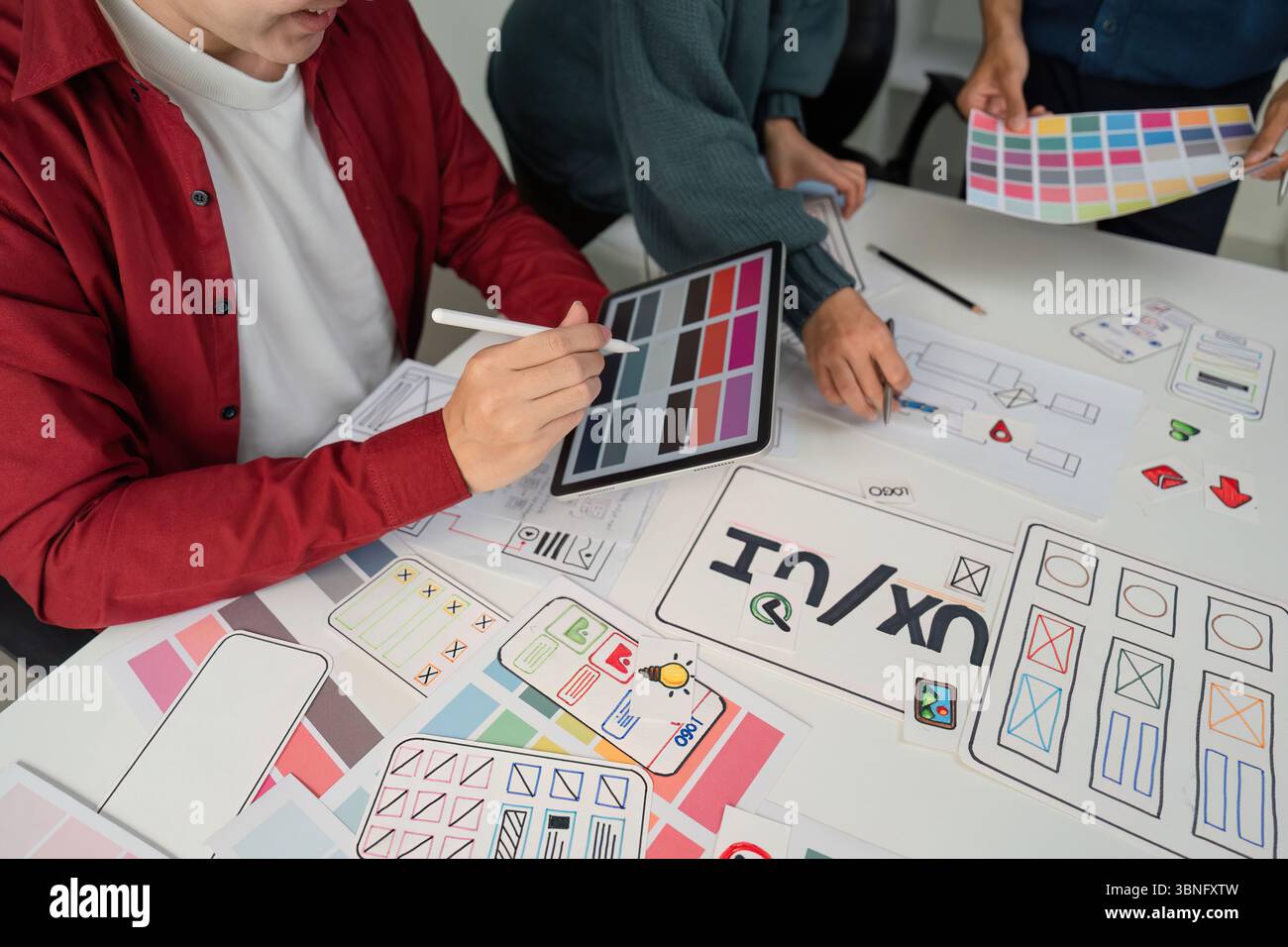 Creative Collaboration and Design Prototyping. Team members engaged in a lively session, refining design ideas using digital tools and paper Stock Photo