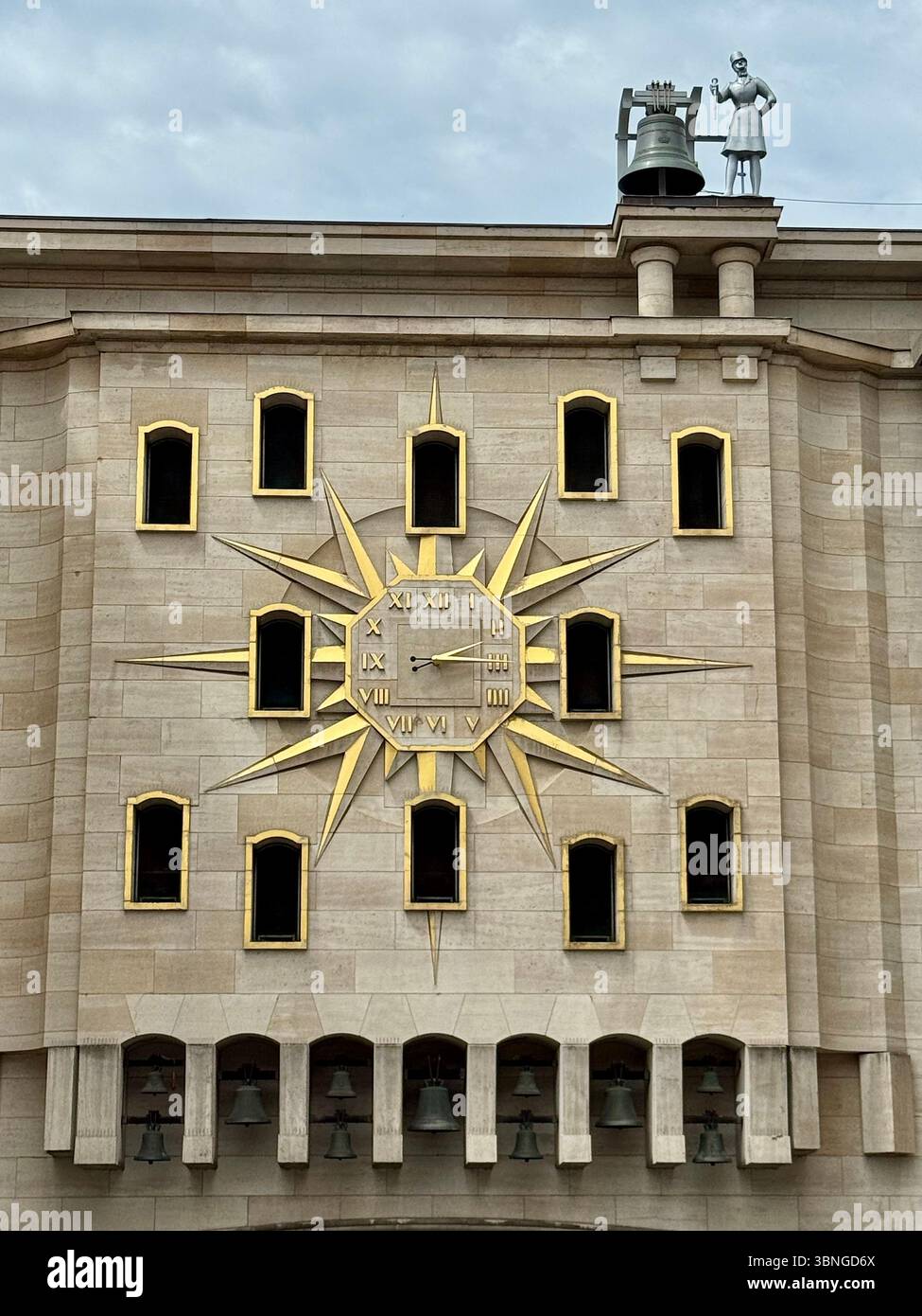 Golden sunburst clock and figurative bell sculpture on the façade of a Brussels public building, Belgium. - Smartphone Captured Stock Image