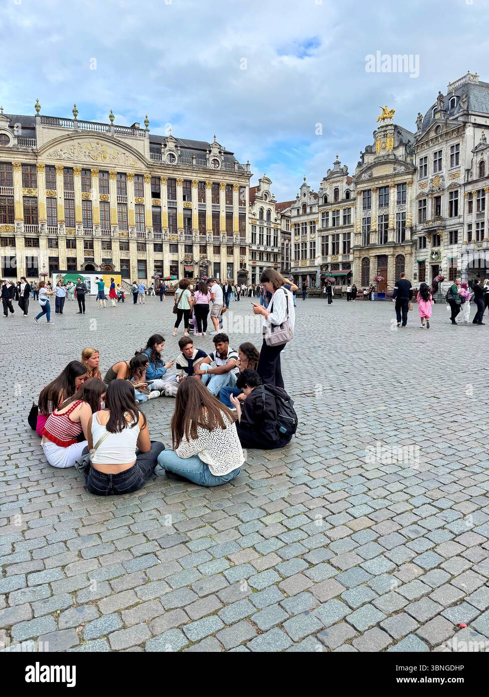 Group of young tourists resting on the cobbles of Brussels’ Grand-Place in front of ornate guildhalls. - Smartphone Captured Stock Image