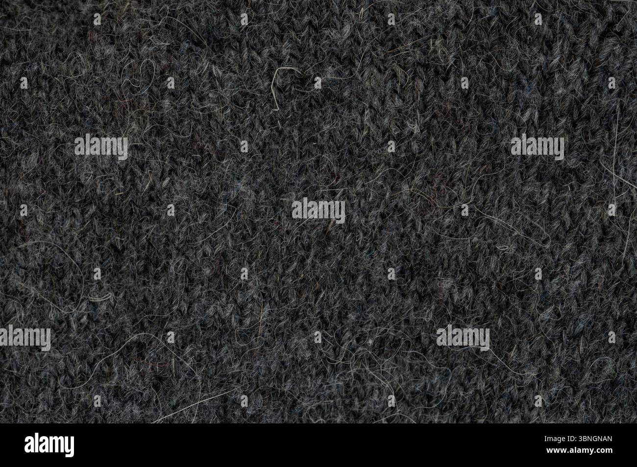 Close view of dark gray knitted fabric reveals intricate texture and fine fibers, highlighting textile craftsmanship. Stock Photo
