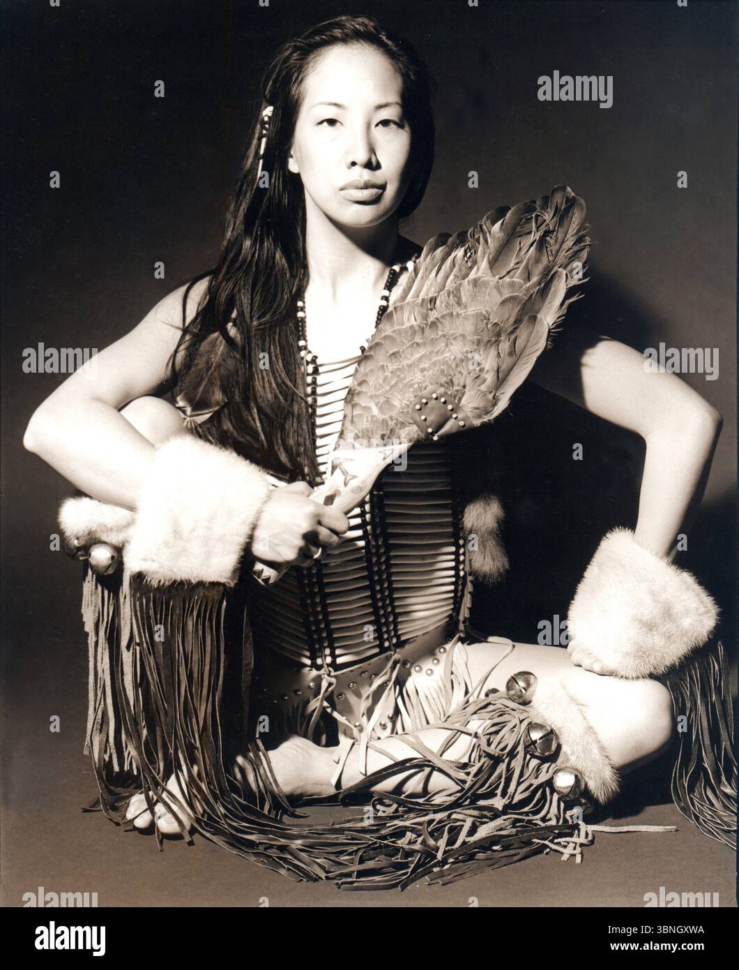 Young woman in native American clothes sitting cross-legged in studio. Stock Photo
