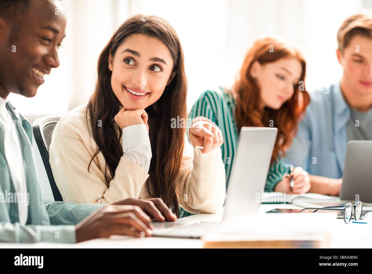 Smiling diverse students sitting at desk working on group project Stock Photo