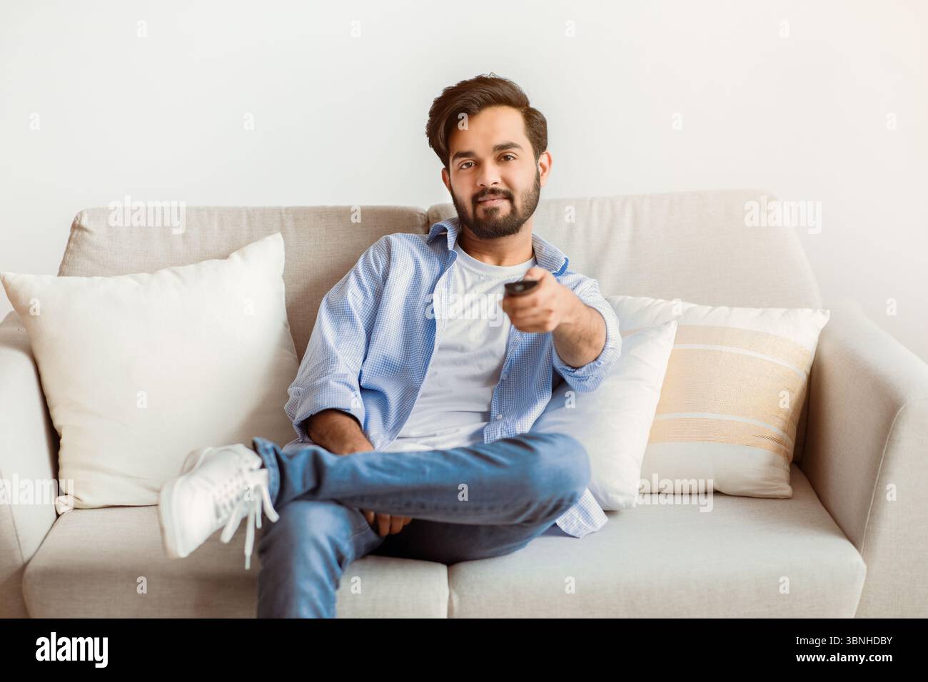 Smiling Young Middle Eastern Guy Watching TV At Home. Stock Photo