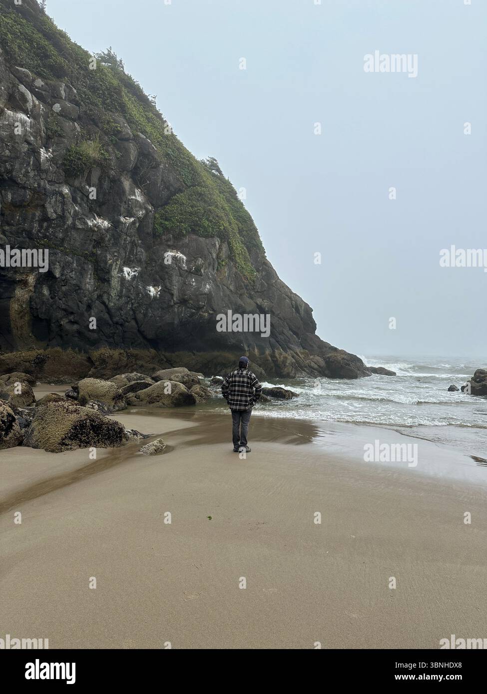 A man, seen from behind,  in a flannel shirt standing on a foggy misty grey beach on the Oregon coast. - Smartphone Captured Stock Image