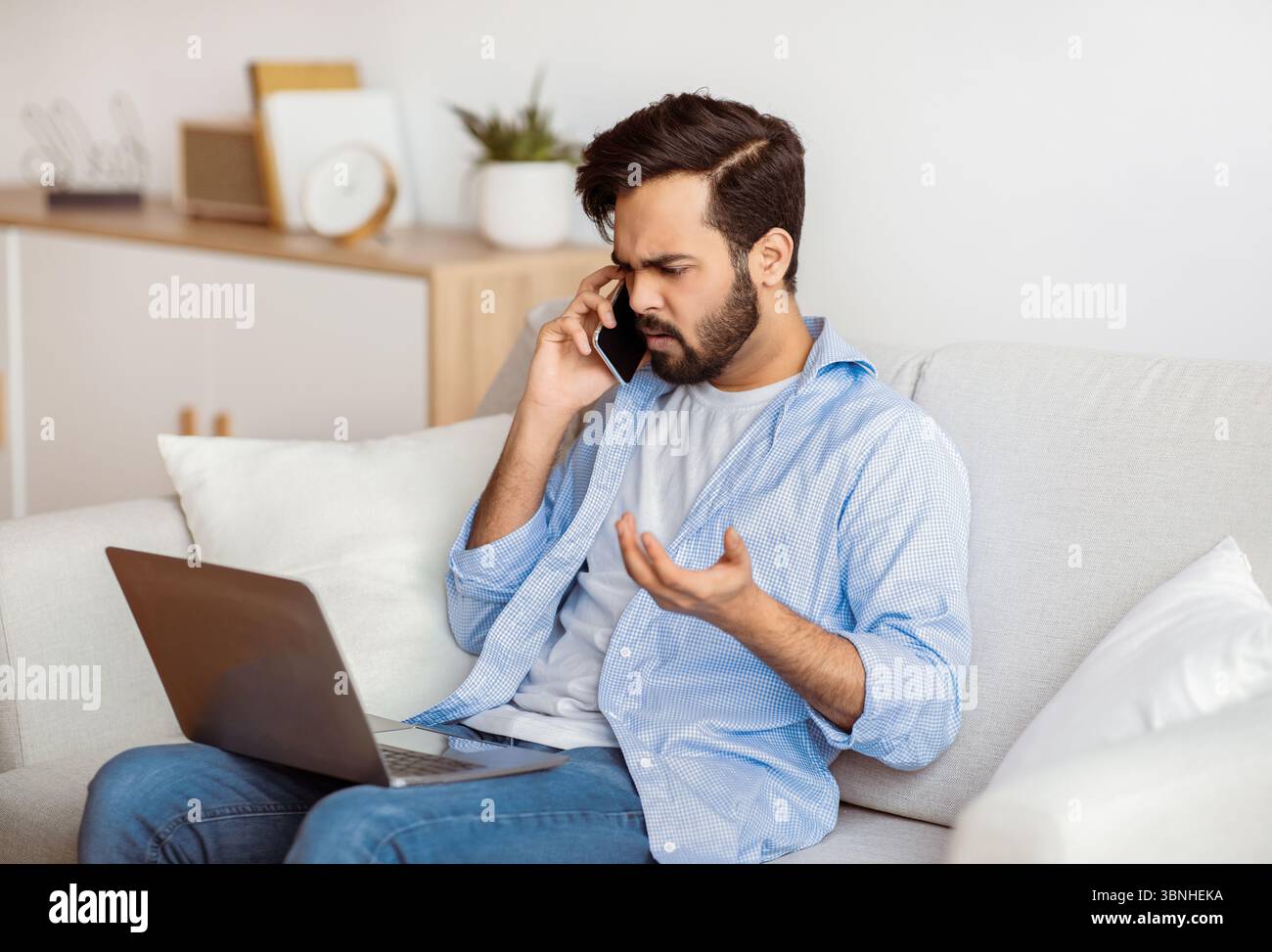 Computer Problems. Frustrated arab guy using cellphone and looking on laptop screen Stock Photo