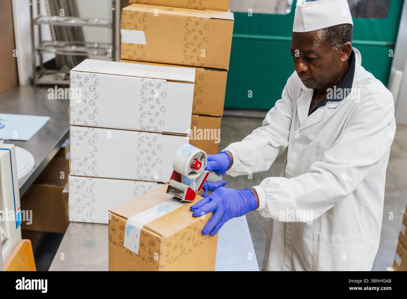 Warehouse worker sealing a cardboard box with tape during packaging process. Stock Photo
