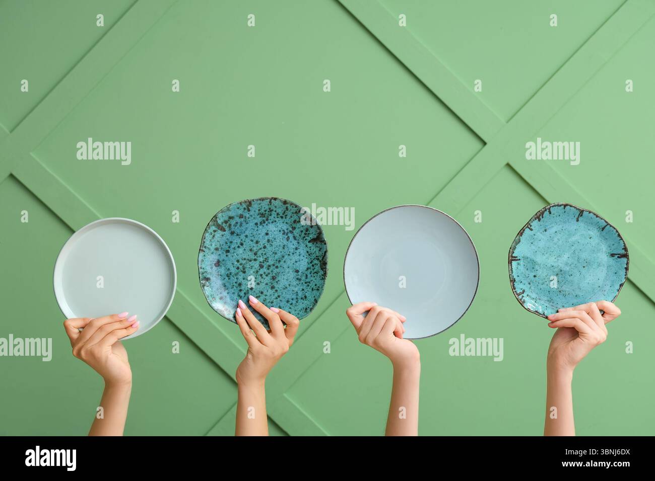 Hands holding empty plates on green background Stock Photo