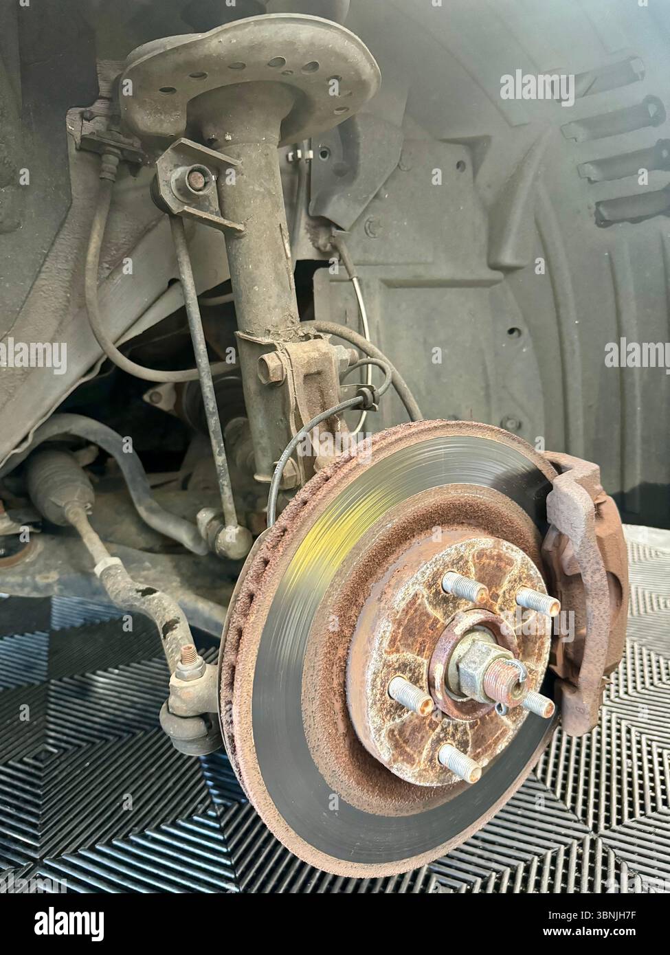 Rusty brake disc and exposed suspension strut on a vehicle wheel hub during repair. - Smartphone Captured Stock Image