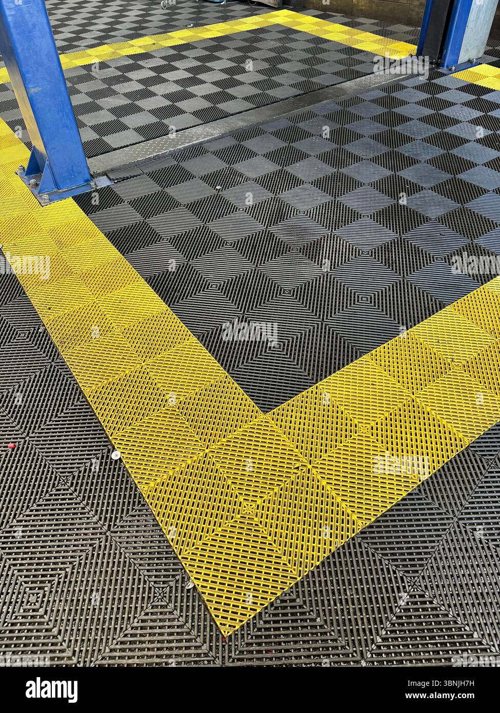 Interlocking safety floor tiles with bold yellow hazard markings in an industrial or workshop setting. - Smartphone Captured Stock Image