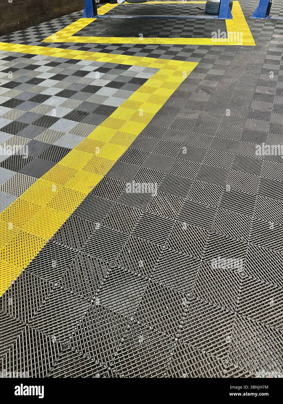 Interlocking safety floor tiles with bold yellow hazard markings in an industrial or workshop setting. - Smartphone Captured Stock Image