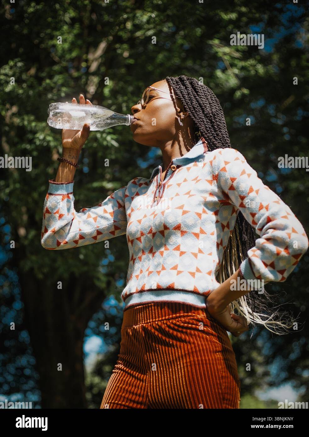 A woman enjoys a summer day in nature, refreshing herself by drinking ...