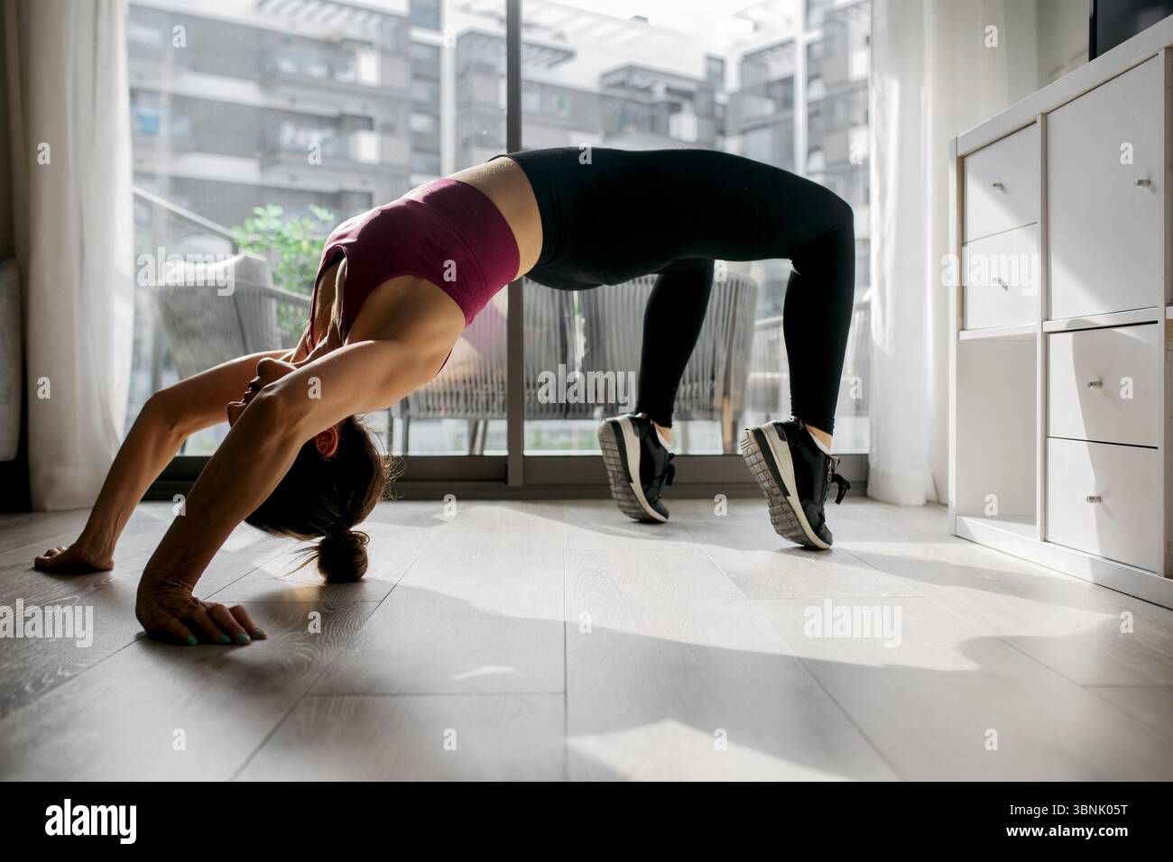 Woman practicing a backbend yoga pose in a bright living room. She ...