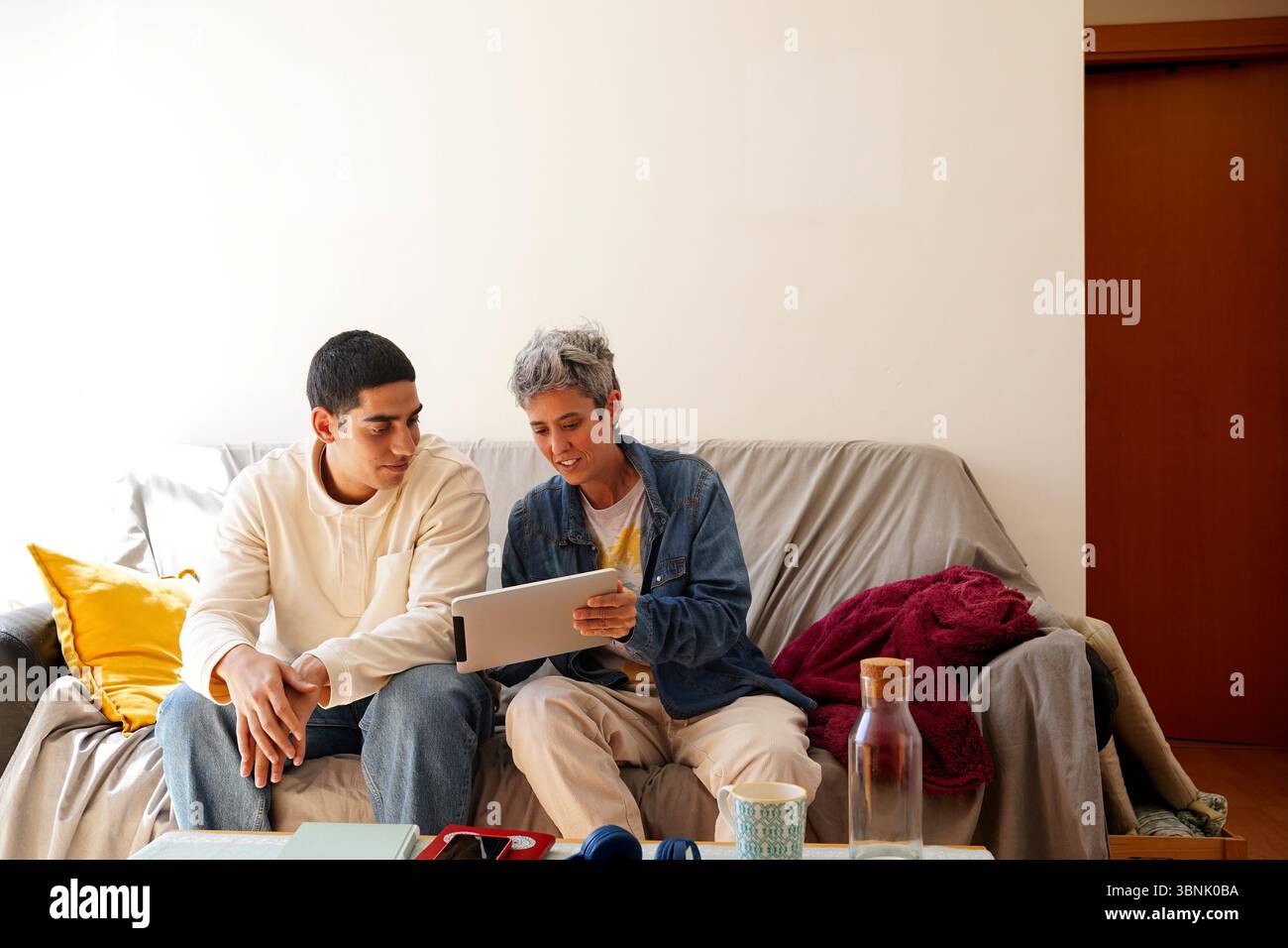 A young Arab man is seated on a cozy couch, engaging in his daily routine while sharing an interactive moment with a friend, surrounded by a warm and Stock Photo