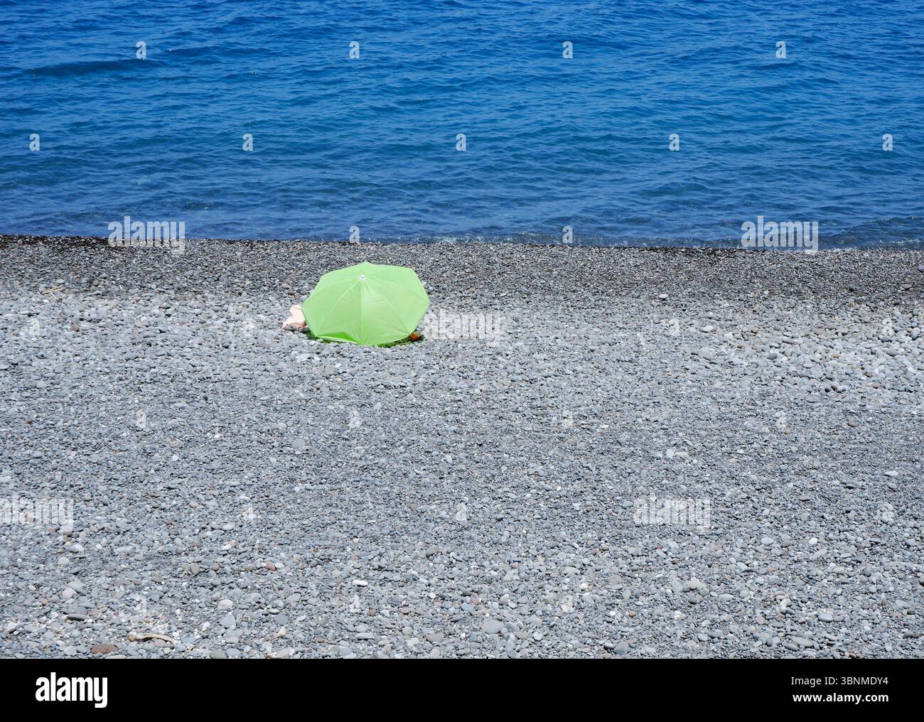 green parasol on a pebbled beach Stock Photo