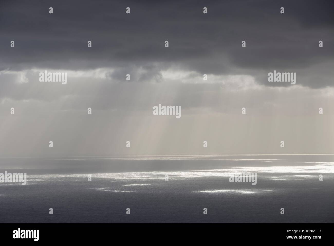 Rays of light shine through a gap in the clouds and reflect on the sea surface Stock Photo