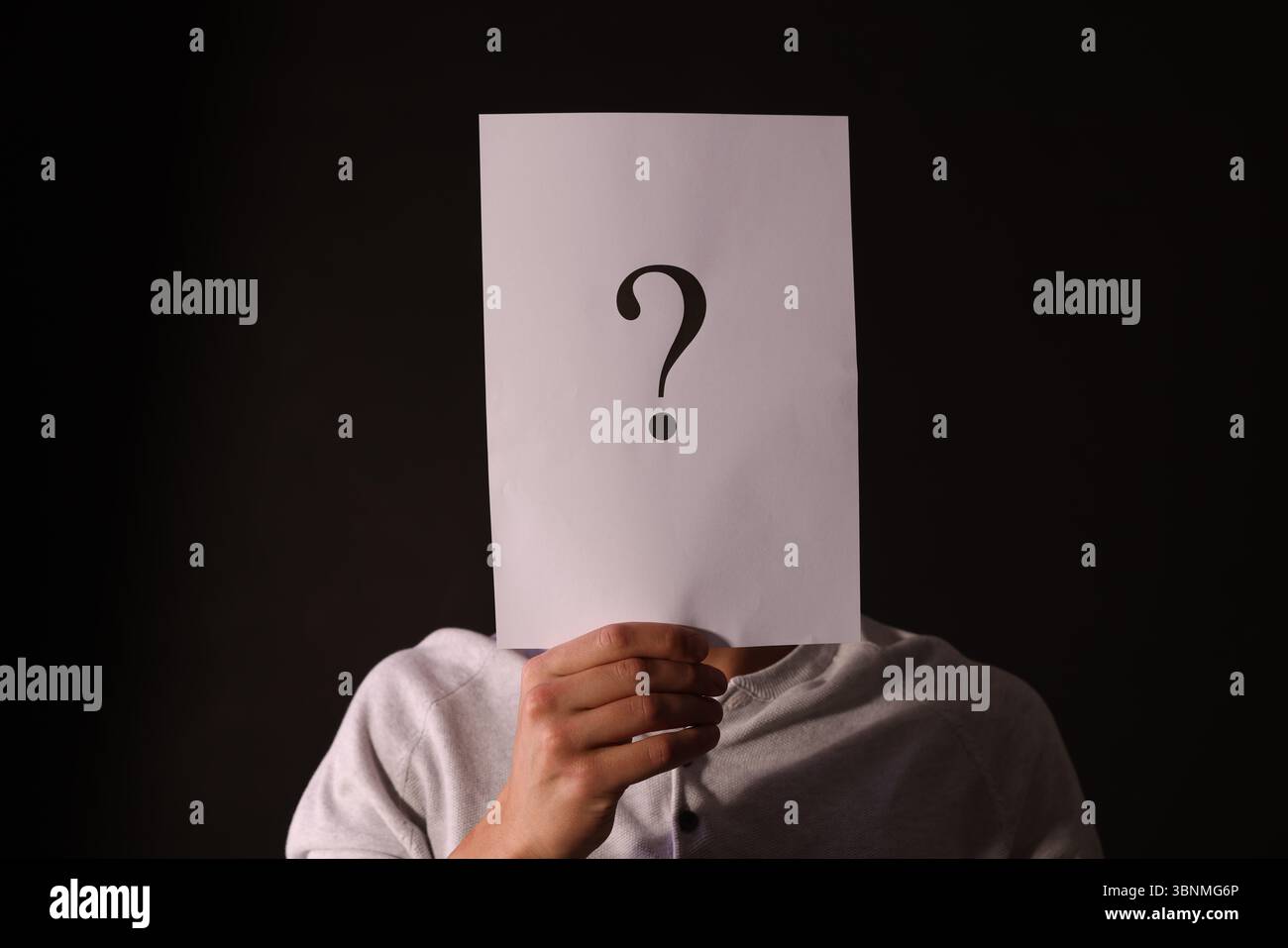 Man hiding behind paper sheet with question mark on dark background Stock Photo