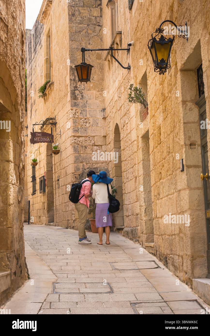 Tourist couple Europe, rear view of two young people in a narrow street checking their location inside the scenic walled city of Mdina, Malta. Stock Photo