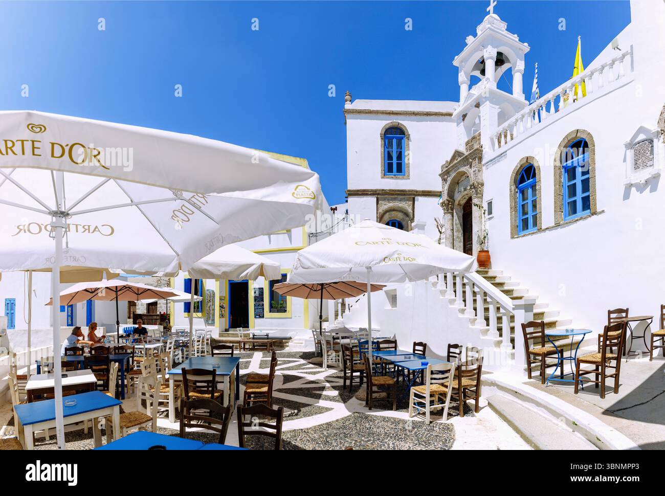 Village square with pebble mosaics, cafe and church of the Assumption of the Virgin Mary in the mountain village of Nikia on the island of Nissyros (Nisyros, Nissiros, Nisiros) in Greece Stock Photo