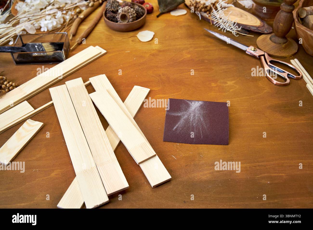 Woodworking workspace with light wooden planks, sanding paper, dried flowers, and tools. DIY project preparation for a natural decorative collage or Stock Photo