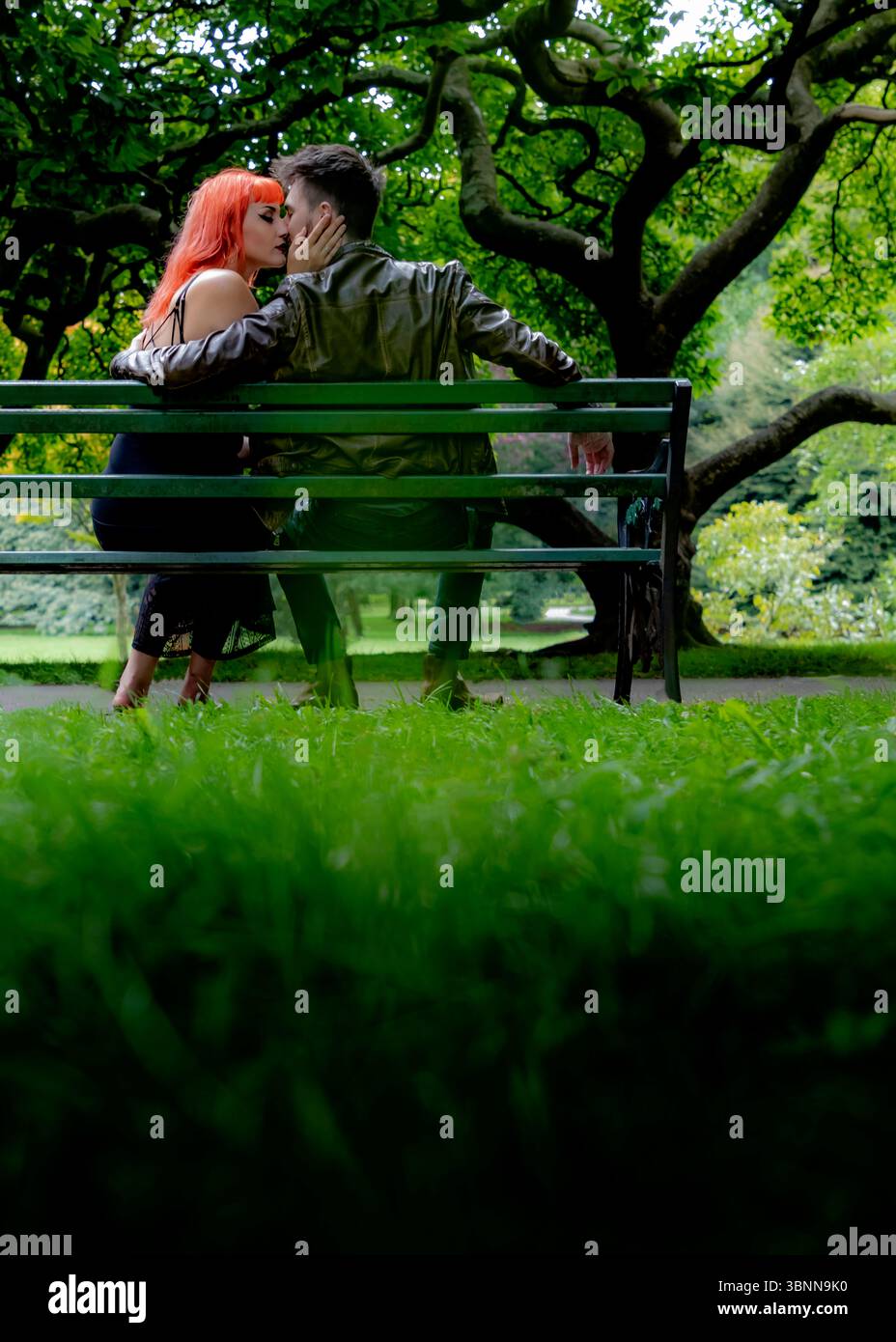 A couple is sitting on a park bench, sharing a kiss. The woman has ...