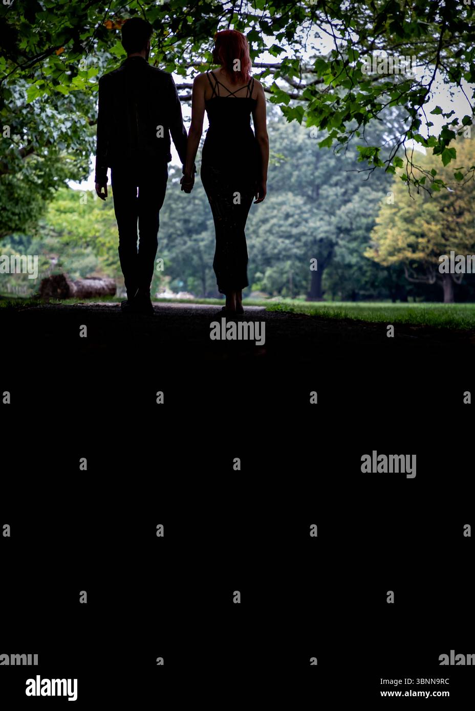 A couple walks hand-in-hand down a path in a park. Stock Photo